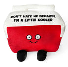 A cooler plushie with a white top and red bottom. The white top features black embroidered text that says, "Don't hate me because I'm a little cooler." The red section has a smiling face, with black legs sticking out from the bottom.