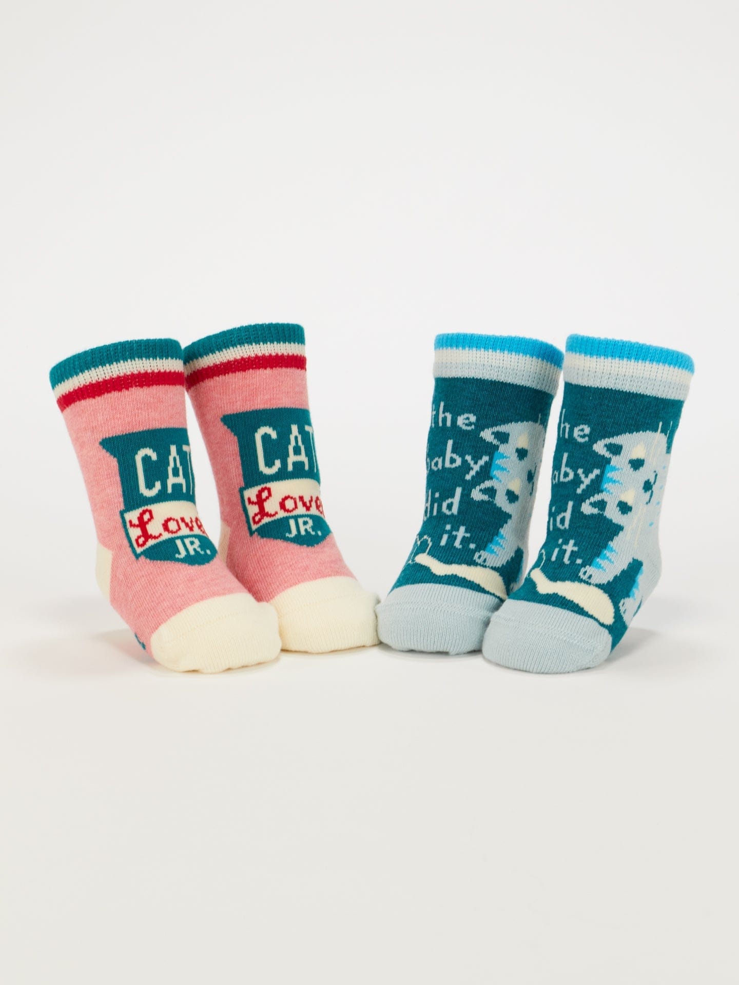 Two pairs of Blue Q baby socks; one pair is pink and teal with 'Cat Lover JR.' and a cat face, the other is teal and white with the text 'the baby did it.' and a cat illustration.