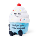 A cupcake plush with white frosting, rainbow sprinkles, and a blue base. The top features a sly, smiling face, while the bottom has black embroidered text that reads, "I baked you some shut the fucupcakes." Black legs sticking out the bottom and a red cherry on top.