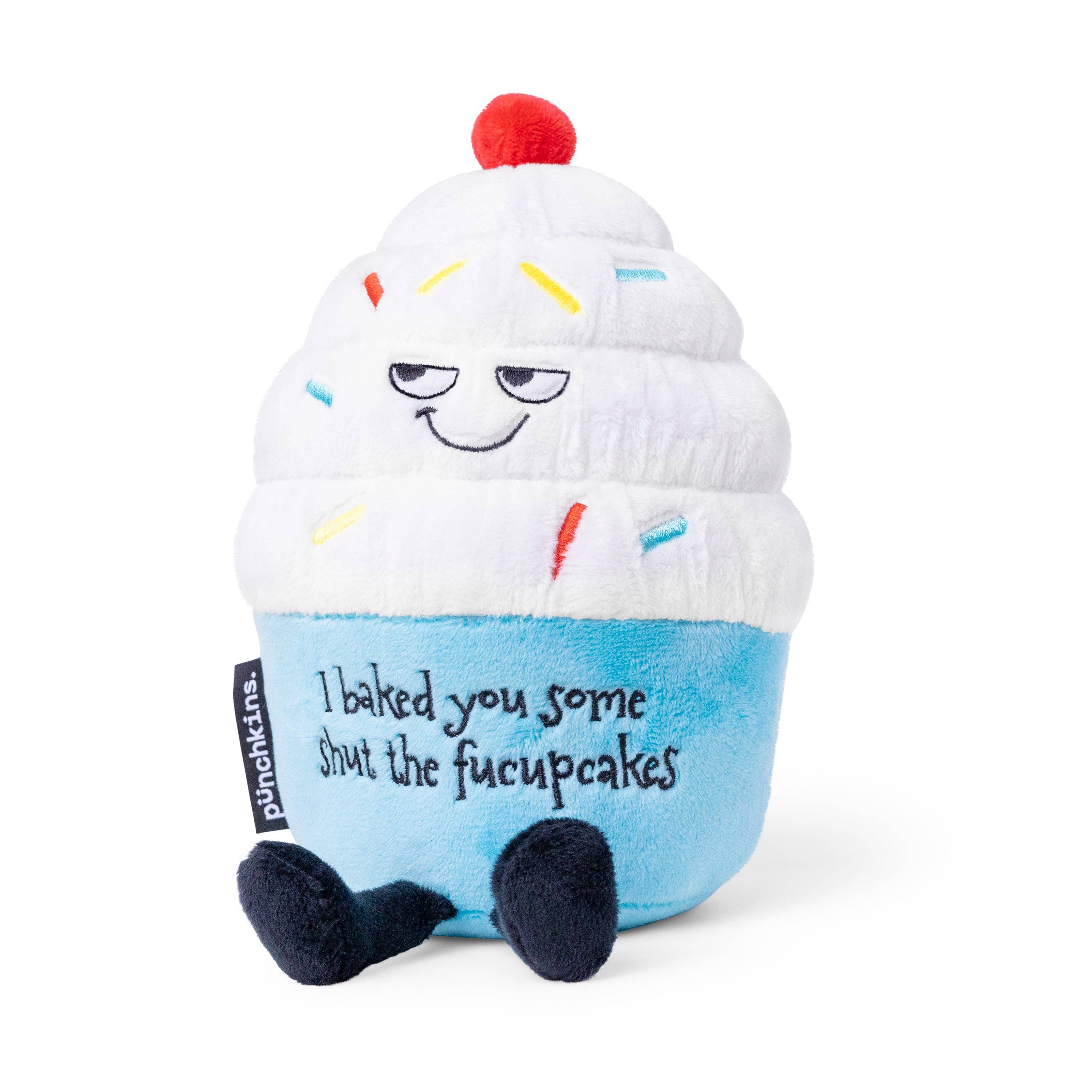 A cupcake plush with white frosting, rainbow sprinkles, and a blue base. The top features a sly, smiling face, while the bottom has black embroidered text that reads, "I baked you some shut the fucupcakes." Black legs sticking out the bottom and a red cherry on top.