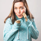 A woman in a teal hoodie playfully uses tiny plastic hands on her fingers, creating a humorous expression. She has a surprised look, enhancing the fun mood.