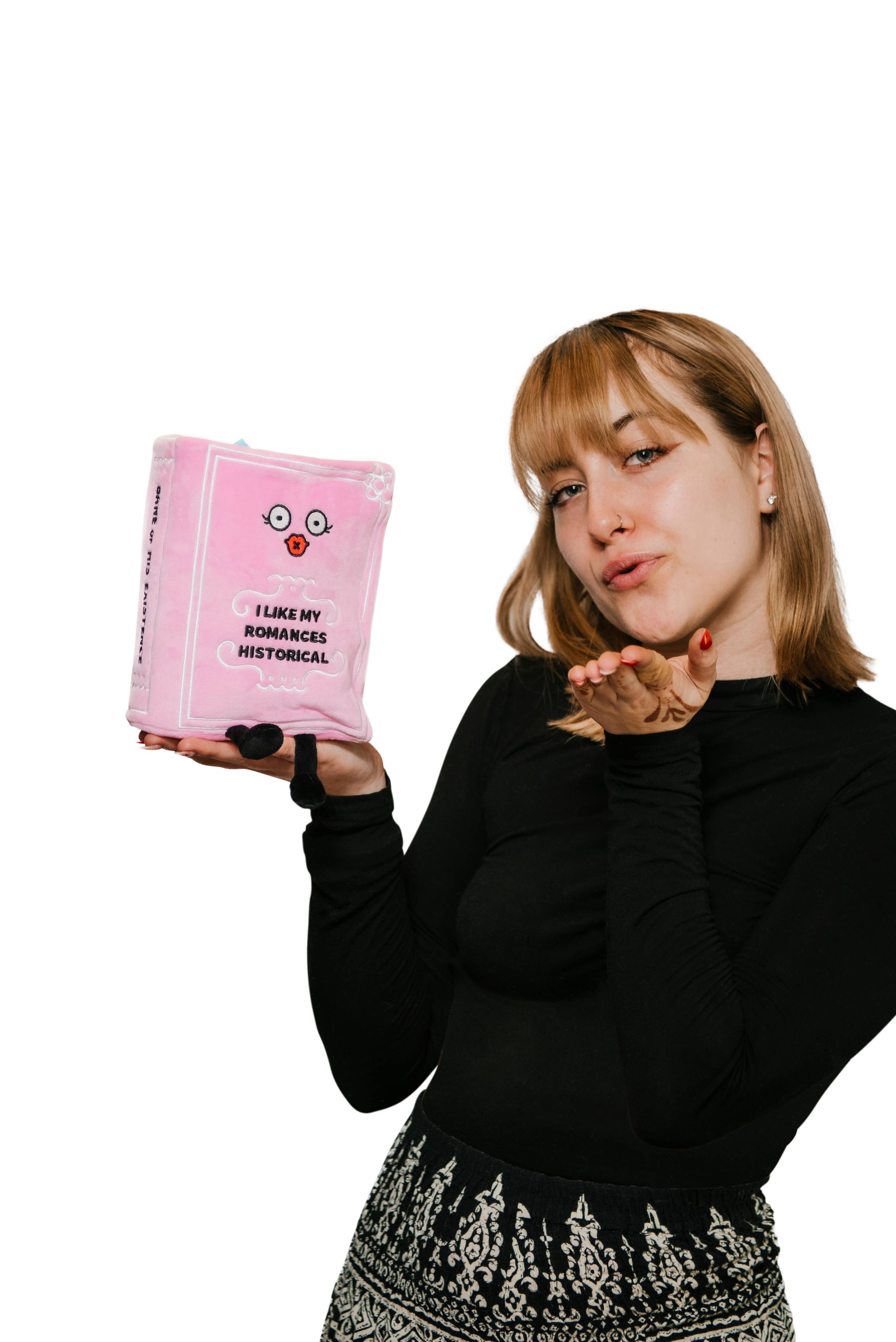 Light pink plush book sitting up with kissy face and black embroidered words that say 'I like my romances historical.' Black legs sticking out bottom and a blue bookmark peeking out the top. A woman is holding the book in her right hand while blowing a kiss with left hand.