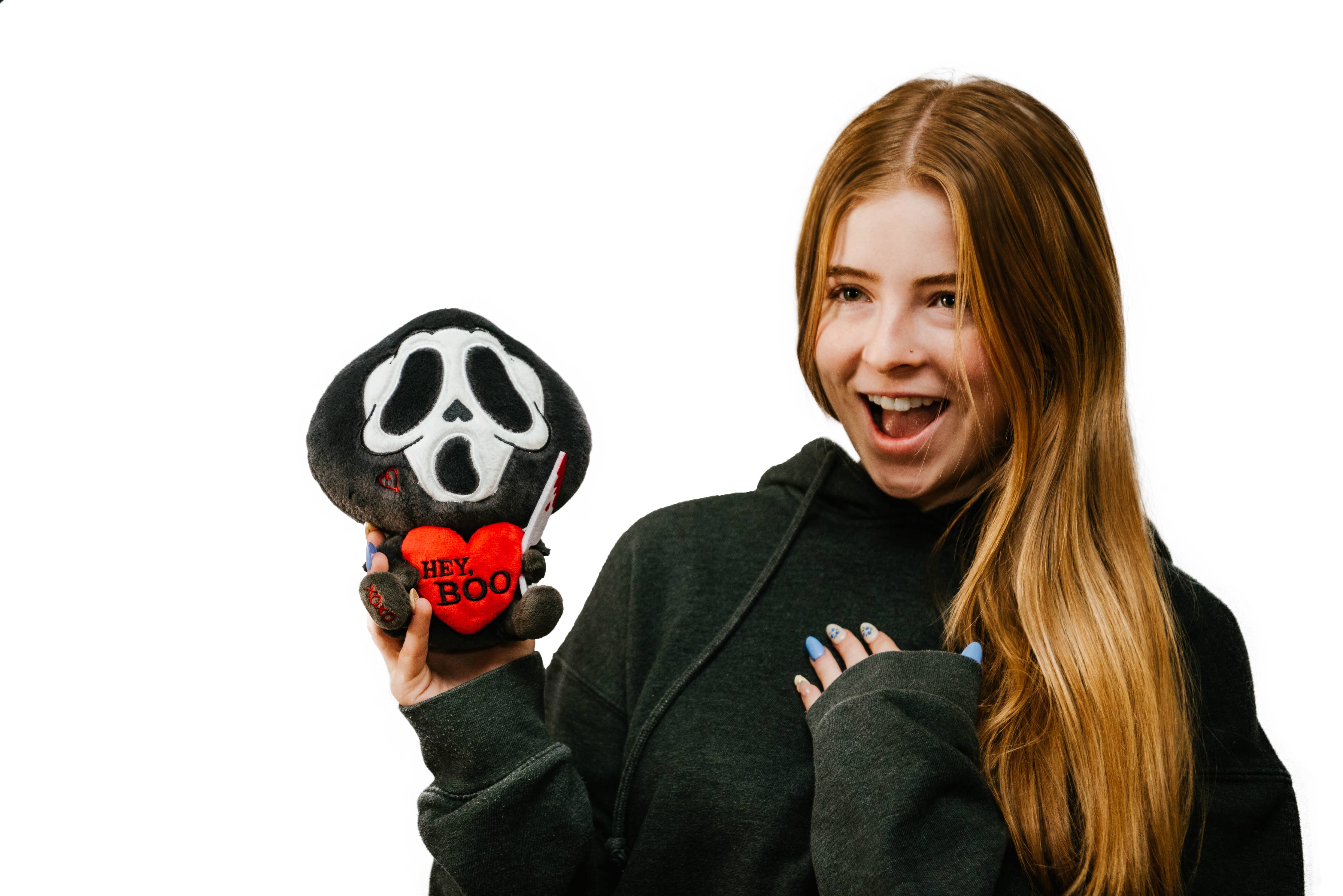 A black and white ghost resembling the Scream mask, holding a bloody knife in one hand and a red heart in the other. The heart has the phrase "Hey, Boo" written in black text.