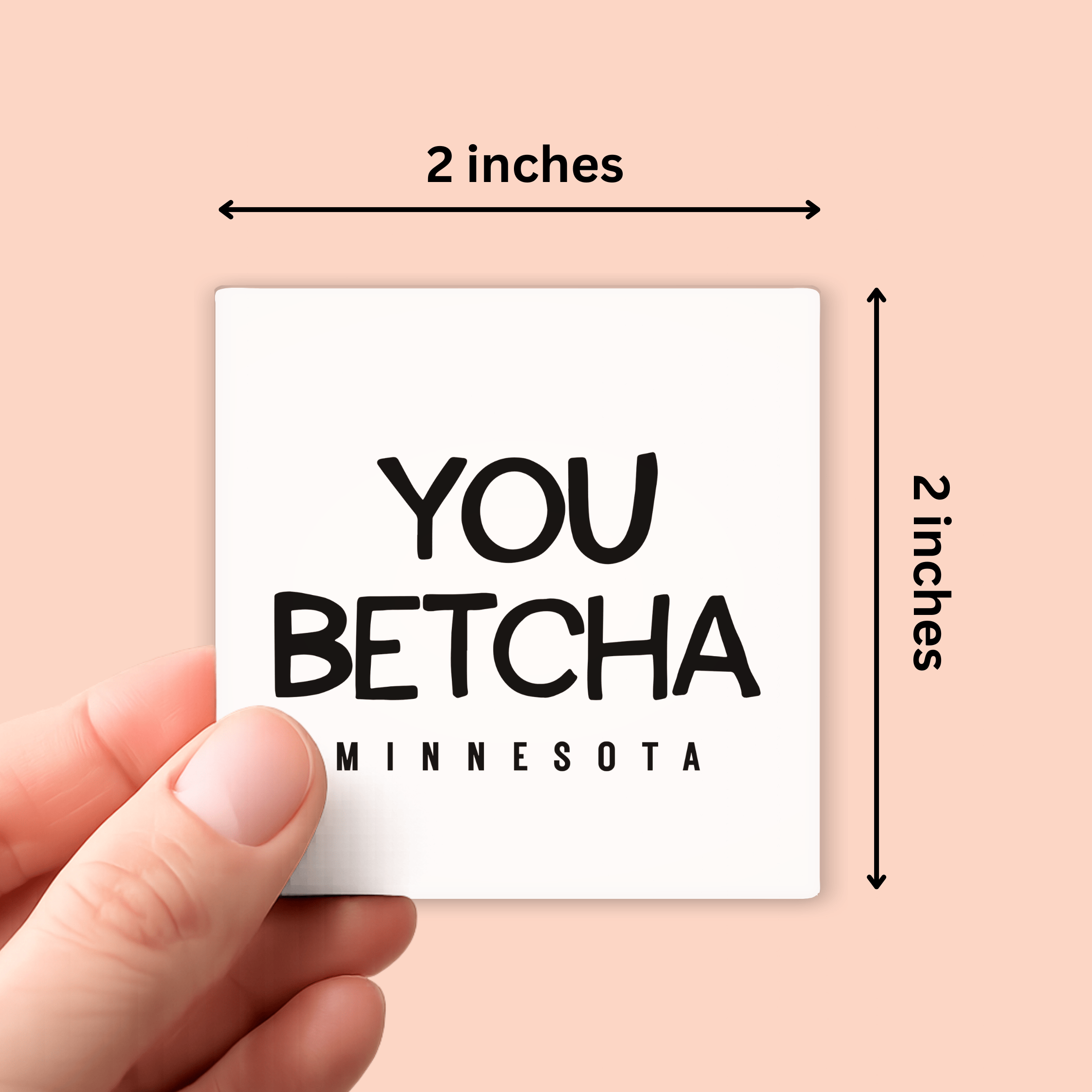 A hand holds a square white magnet with black text reading 'YOU BETCHA MINNESOTA' against a peach background, with dimension arrows indicating the sticker is 2 inches by 2 inches.