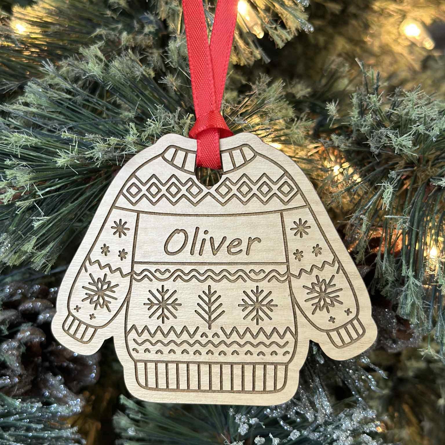 Wooden ornament shaped like a sweater with 'Oliver' on it, hanging on a Christmas tree.