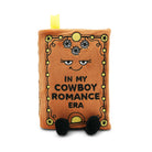 Plush toy resembling a book with a face and text 'In my cowboy romance era' on a white background