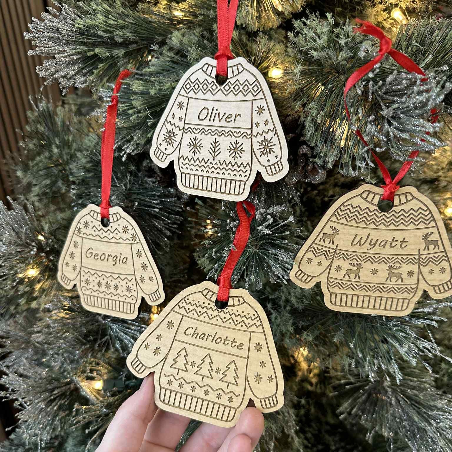 Decorative Christmas ornaments shaped like sweaters and mittens with names on a tree.