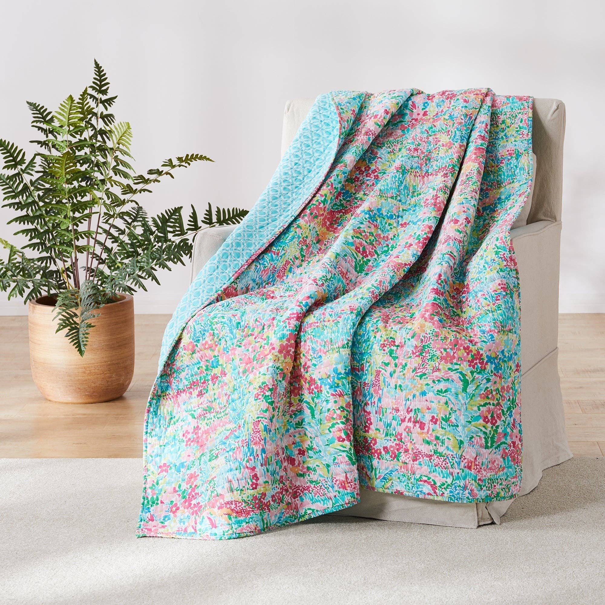Floral patterned blanket draped over a chair next to a potted plant on a wooden floor.
