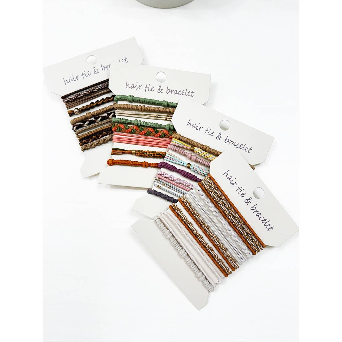 Assorted sets of colorful hair ties and bracelets on white packaging cards labeled "hair tie & bracelet," showcasing various textures and patterns.