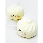 Two off-white dumpling-shaped slow-rising squishy toys with cute, simple anime-style smiley faces, staged on small white display blocks.