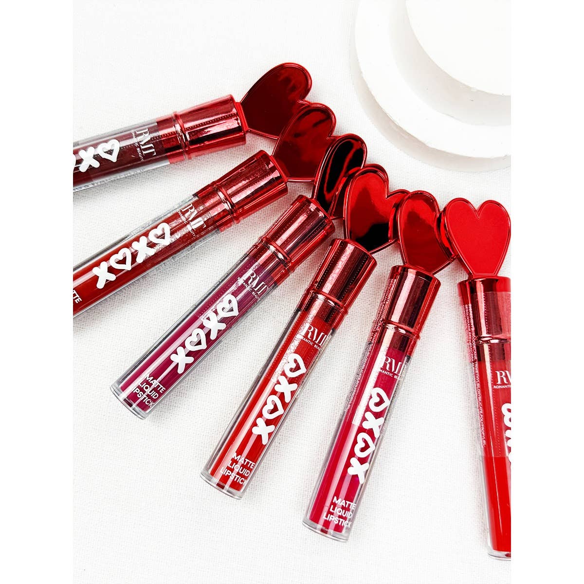 Six tubes of red matte liquid lipstick are laid diagonally on a white surface. They feature heart-shaped caps and the text "XOXO" on the tubes.