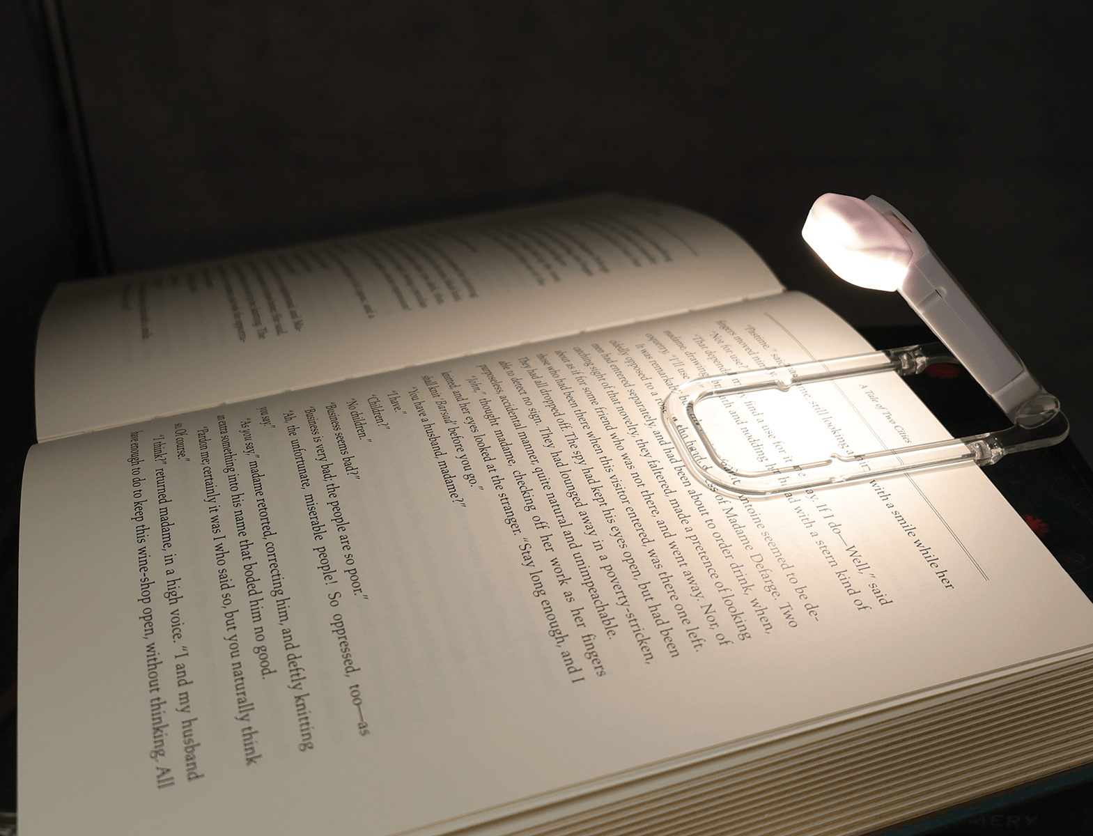 Open book illuminated by a small, clip-on LED reading light. The scene conveys a cozy atmosphere, emphasizing nighttime reading in a dimly lit space.