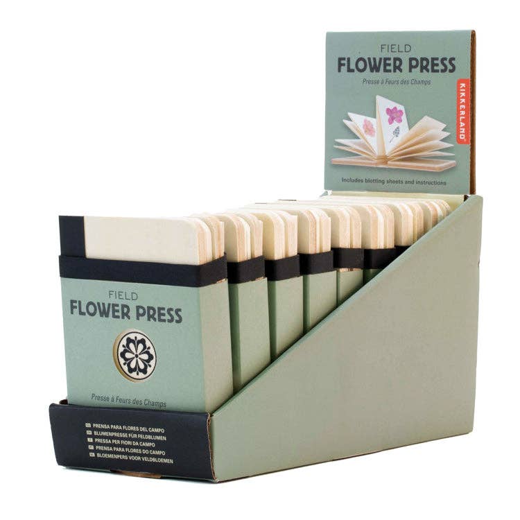 Display of compact accordion-style field flower presses in green packaging, neatly arranged in a retail countertop holder.