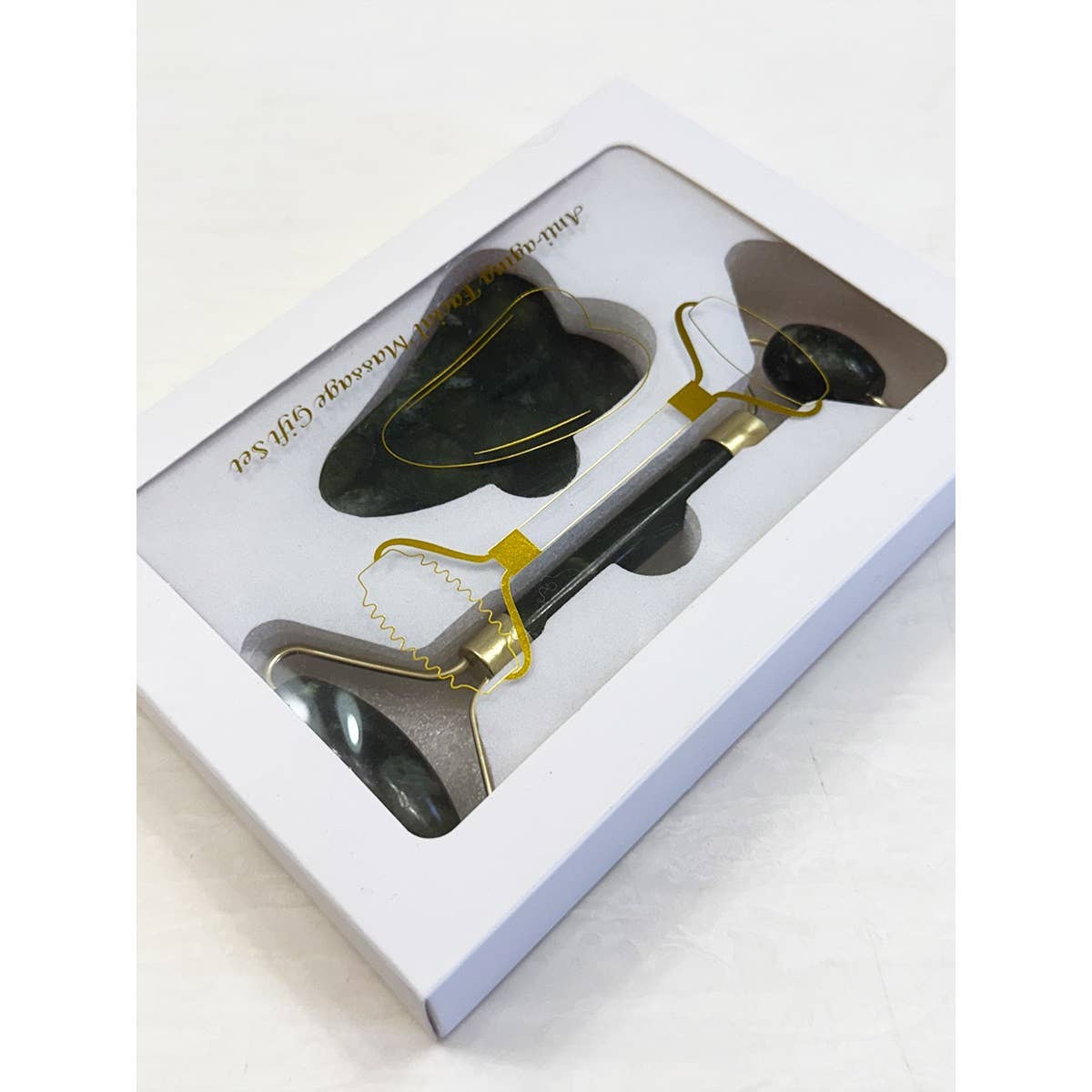 Boxed facial massage set with a black jade roller and heart-shaped gua sha tool, visible through a clear window. The packaging is sleek and elegant.
