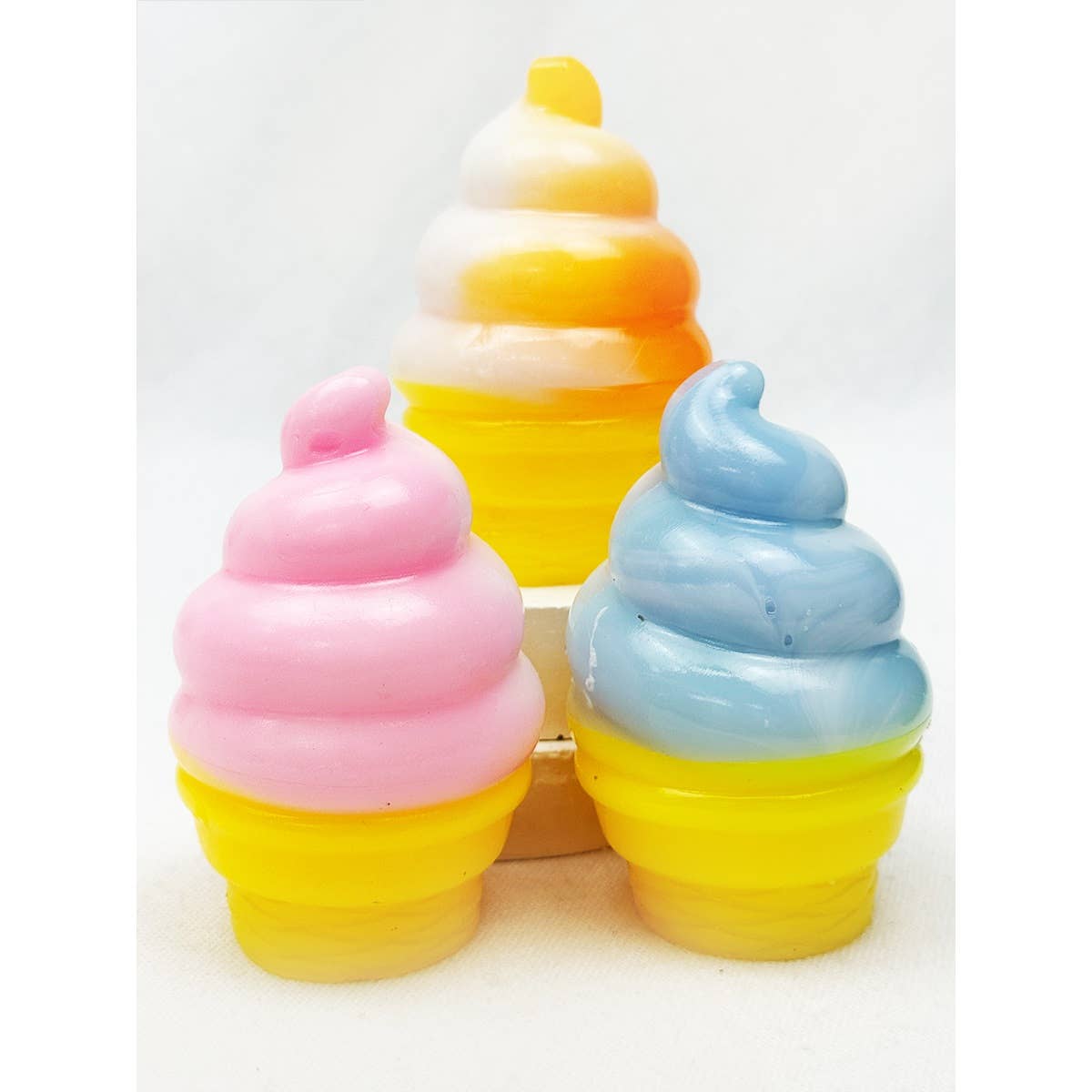 Three soft-serve ice cream cone squeeze squishy toys in pink, blue, and orange/white swirl colors with yellow bases.