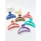 An assortment of seven minimalist matte half moon hair claw clips in a variety of pastel and muted tones, including coral, lavender, turquoise, and tan, arranged neatly together.