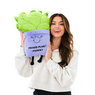 Person holding A soft, plush plant toy featuring a vibrant green plant in a purple pot. The pot has a cheerful, smiling face with closed eyes, and black text on the front reads 'Proud Plant Parent.'