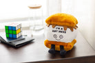 A s'more plushie featuring a smiley face, with black embroidered text that says 'I'm a hot mess.' The plushie has a layer of soft, golden-brown marshmallow, a piece of chocolate, and two graham crackers, all stitched together in a cute, playful design.