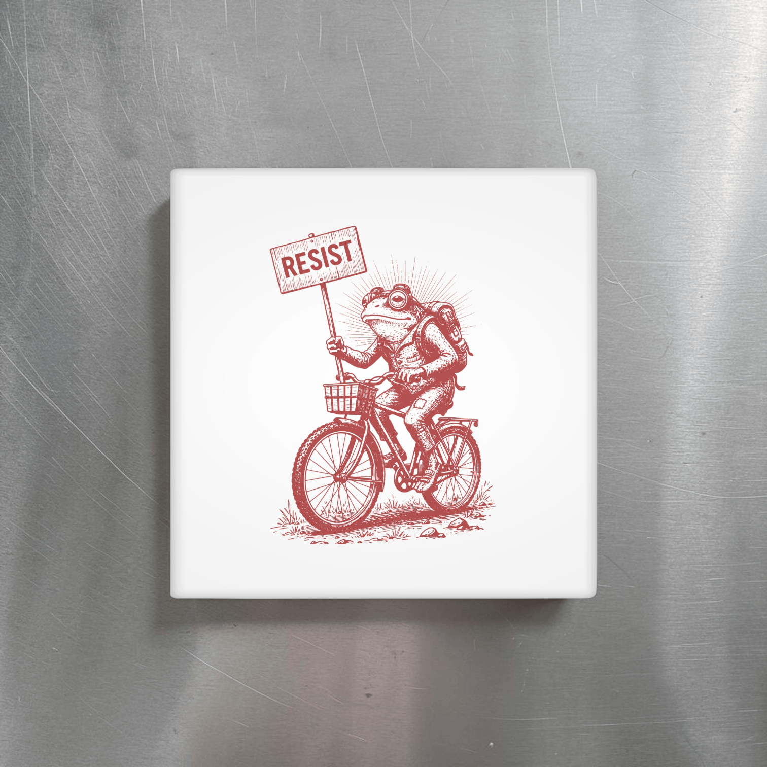 Fridge magnet with a red illustration of a frog on a bicycle holding a 'RESIST' sign, placed on a metallic surface.