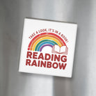 White square magnet with rainbow and text on a metallic surface - Take a Look It's In a Book Reading Rainbow"