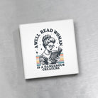 Square magnet with a graphic of a woman reading a book and text 'A well-read woman is a dangerous creature' on a gray background.
