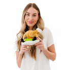 Woman holding A cooked turkey dinner plush on a plate with green lettuce. The turkey has a smiley face with a red tongue sticking out and black text that says "Winner Winner." It also has black legs sticking out.