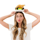 Woman holding on top of her head a A cooked turkey dinner plush on a plate with green lettuce. The turkey has a smiley face with a red tongue sticking out and black text that says "Winner Winner." It also has black legs sticking out.