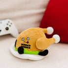 A cooked turkey dinner plush on a plate with green lettuce. The turkey has a smiley face with a red tongue sticking out and black text that says "Winner Winner." It also has black legs sticking out.