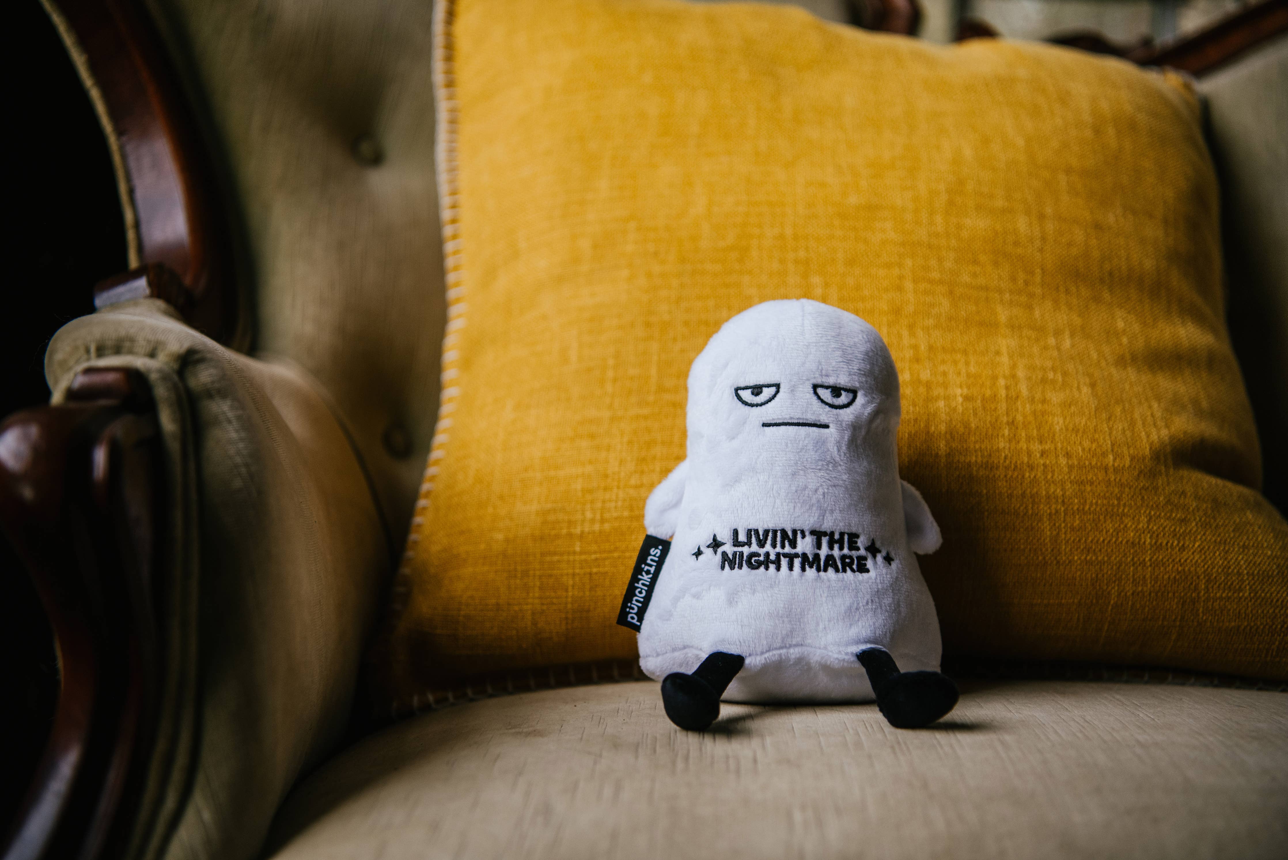 A white ghost plushie with a distressed face and black text that says "Livin' the Nightmare." It has black legs sticking out and black arms at its sides.