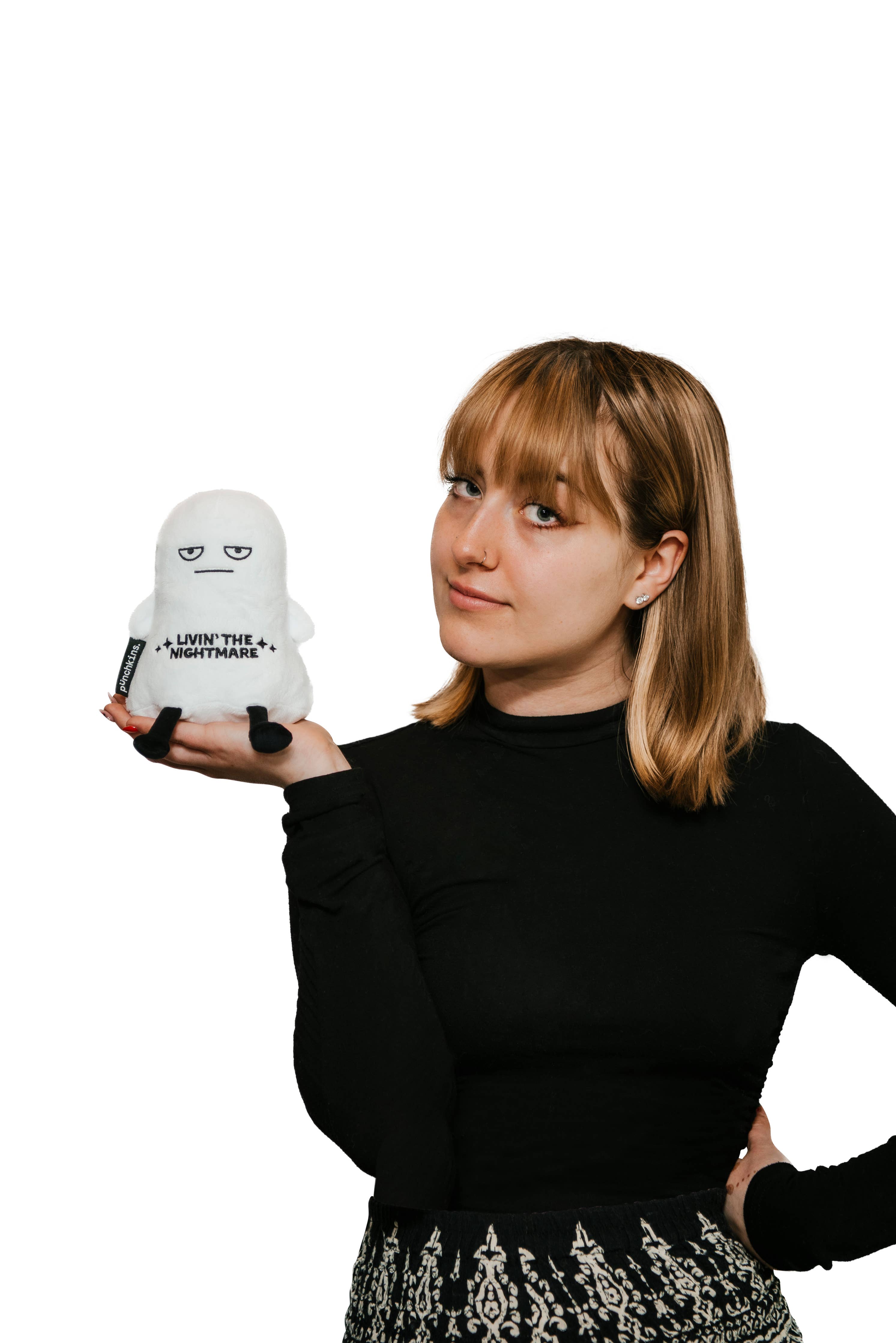 Woman holding a white ghost plushie with a distressed face and black text that says "Livin' the Nightmare." It has black legs sticking out and black arms at its sides.