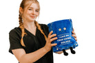 Blue plush book sitting up, with a straight face and white embroidered words that say 'I like my true crimes solved.' Black legs sticking out bottom and black bookmark peeking out the top. Woman is holding the plush