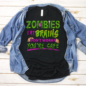 Zombies Eat Brains Don't Worry You're Safe image imprinted on a black shirt. The work Zombies looks like monster lettering with open flesh and bones in a cartoon fashion